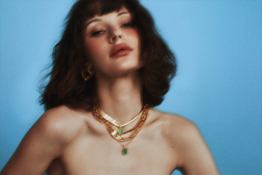 Model with a curly bob against a blue backdrop, wearing two Kathryn pendants layered with gold chains